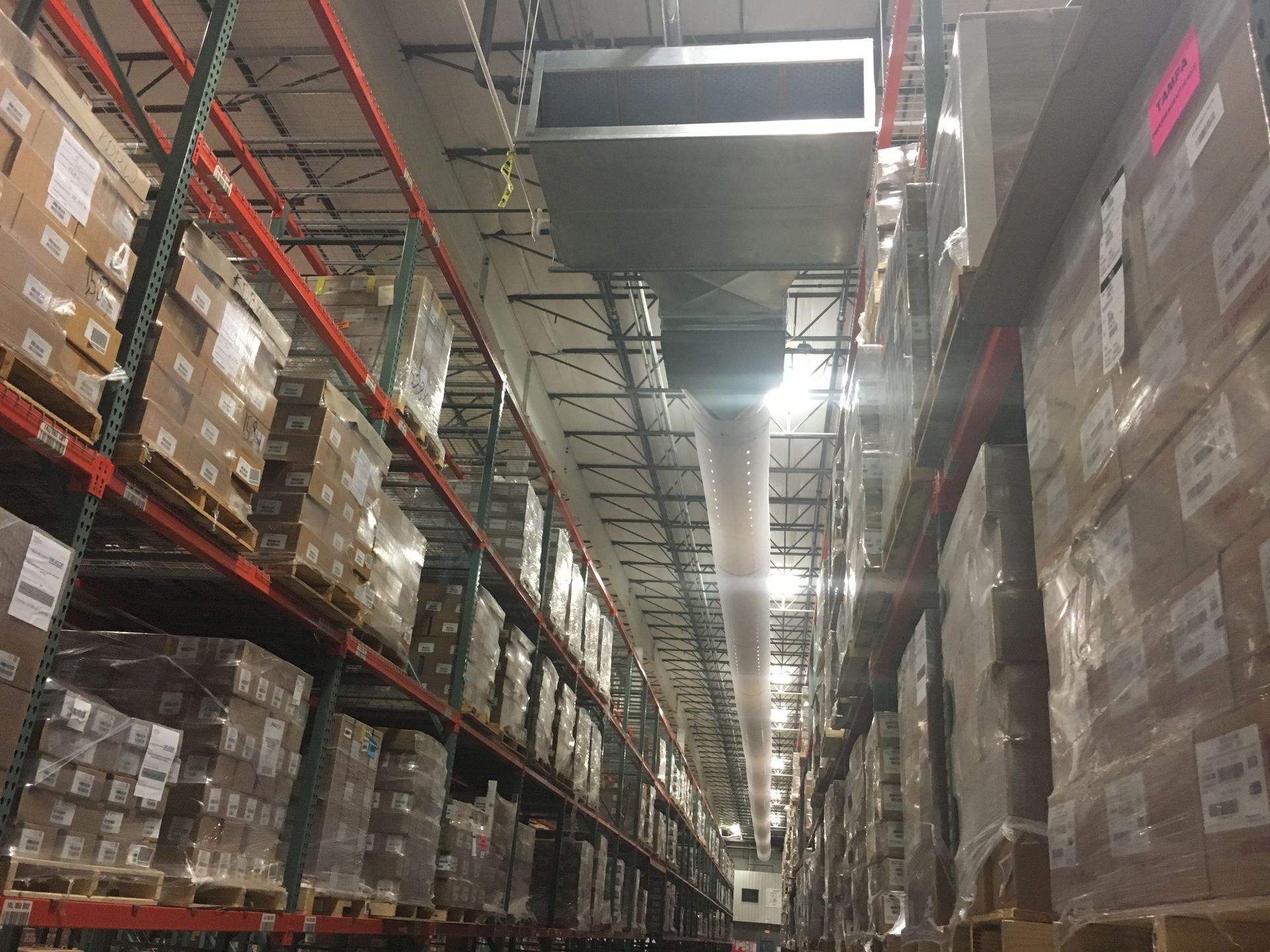 Aisle in a warehouse with tall shelves stacked with boxes under bright overhead lights.