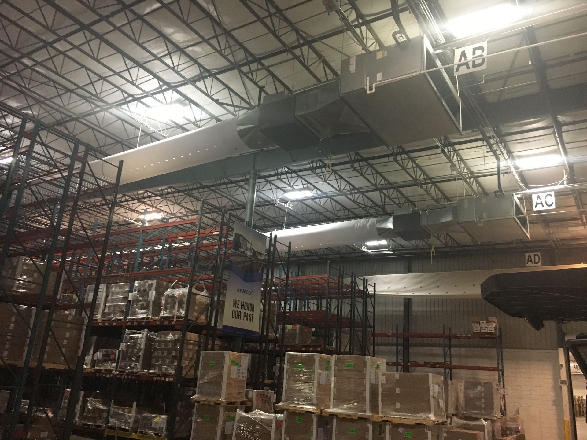 Warehouse interior with stacked boxes, tall shelving, and overhead industrial lights