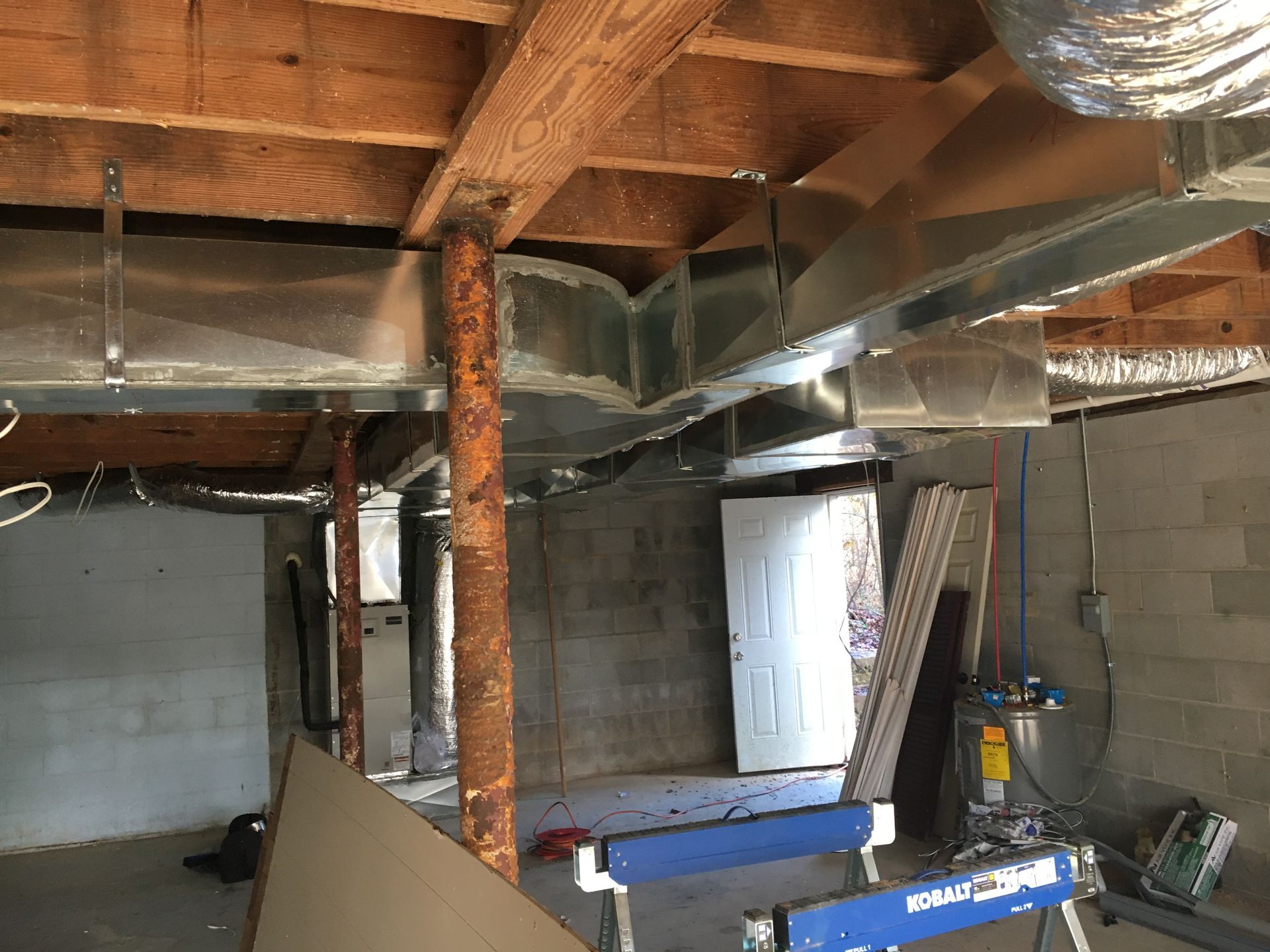 Basement with exposed beams, ducts, cinderblock walls, and construction materials.