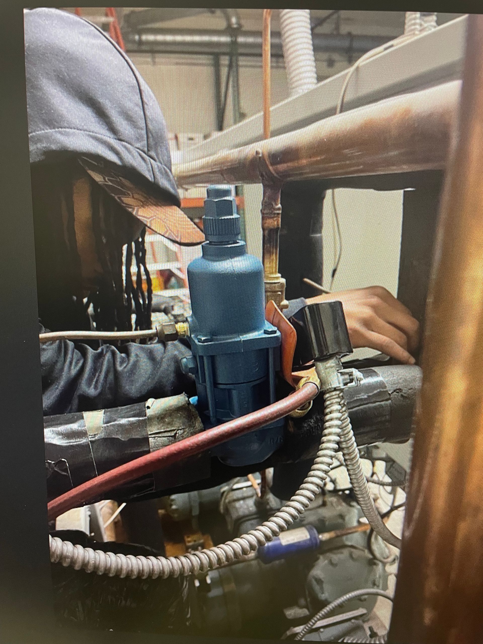 Workers inspecting a blue pipe assembly in an industrial setting, surrounded by hoses and mesh.