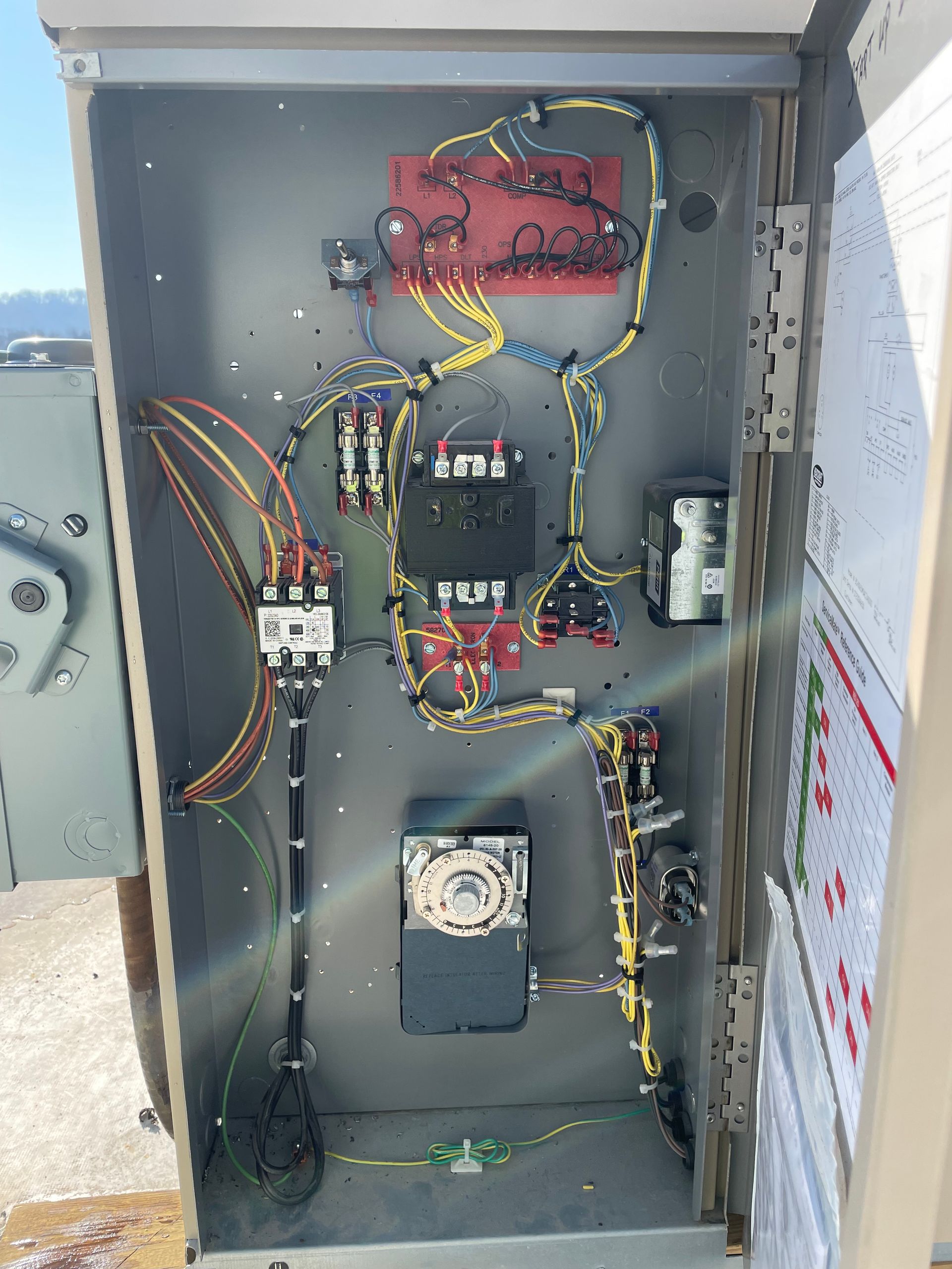 Open electrical control panel with wires, breakers, relays, and a fan inside a gray metal cabinet