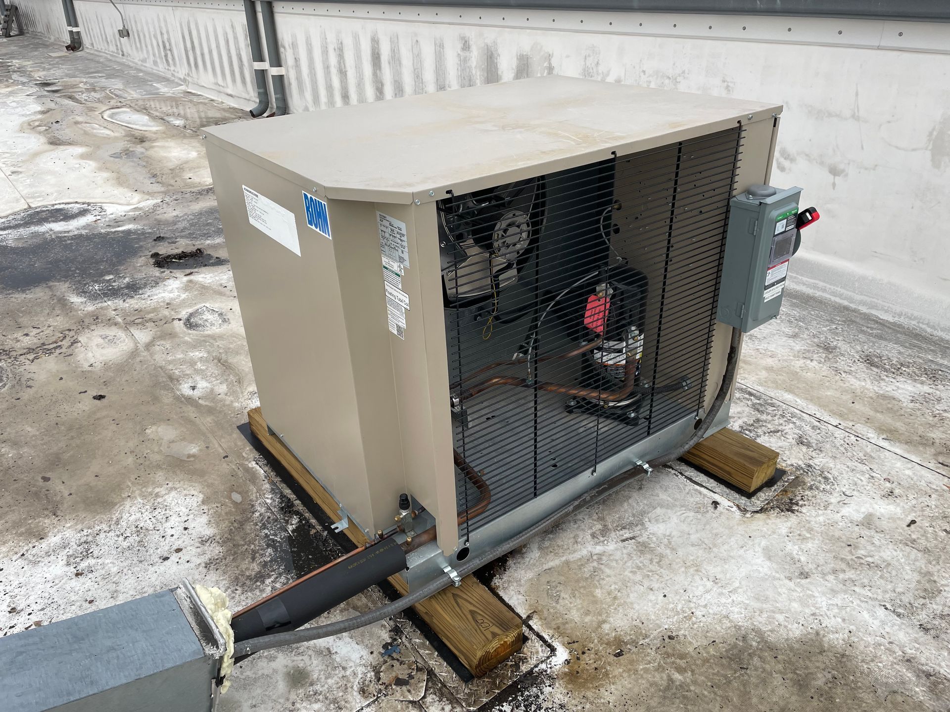 Outdoor HVAC unit on a snowy rooftop with exposed piping and an electrical box