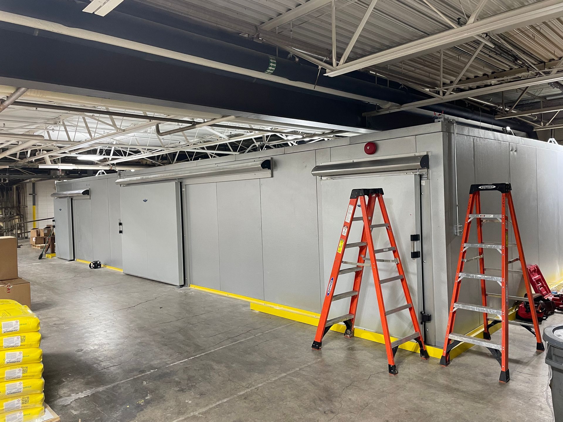 Industrial room with gray walls, exposed ceiling, and two orange ladders on a concrete floor.