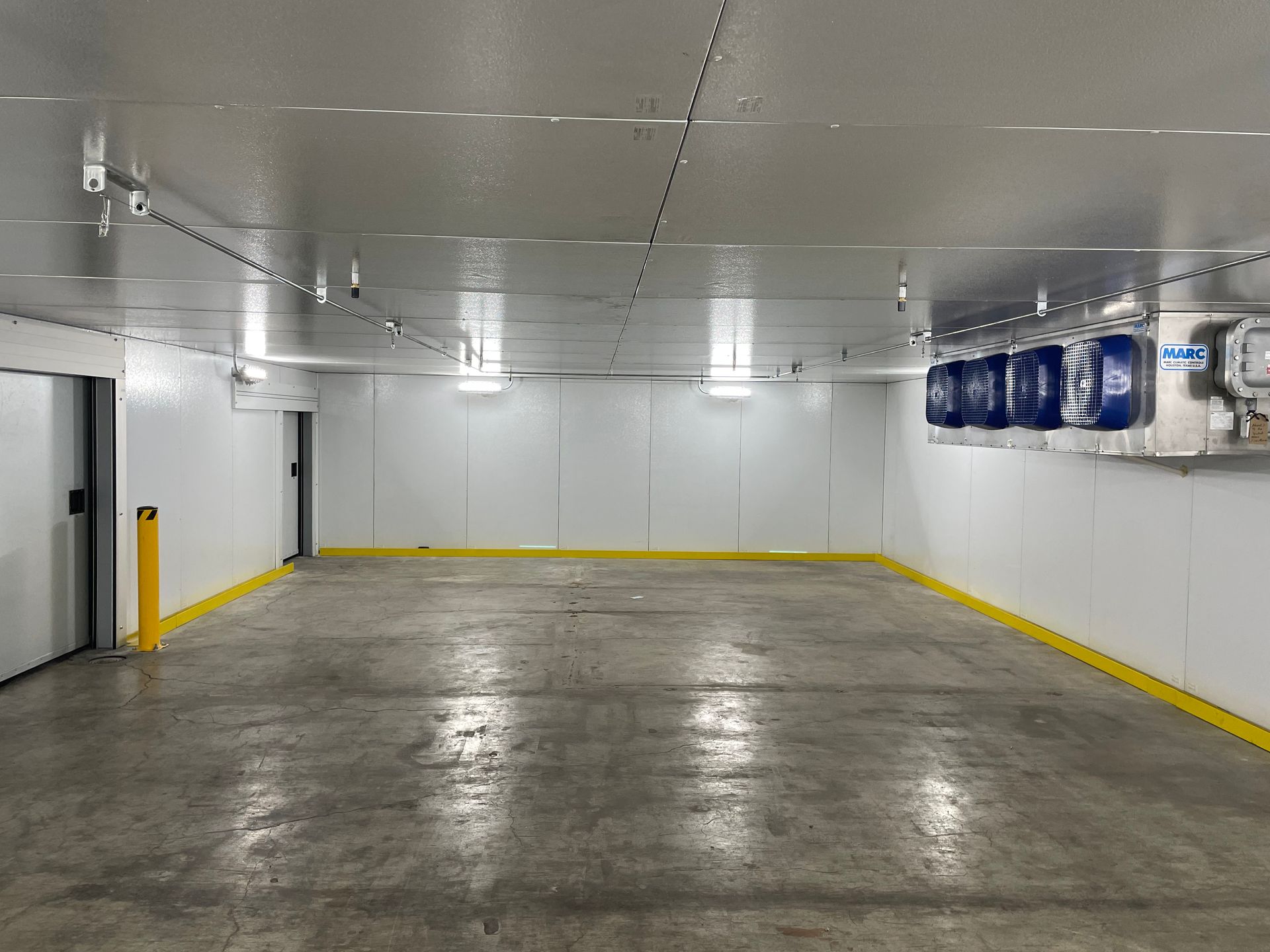 Empty indoor garage with a concrete floor, white ceiling, and yellow safety markings along the walls.