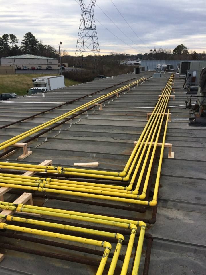 Yellow utility pipes running along a rooftop beside industrial buildings and power lines