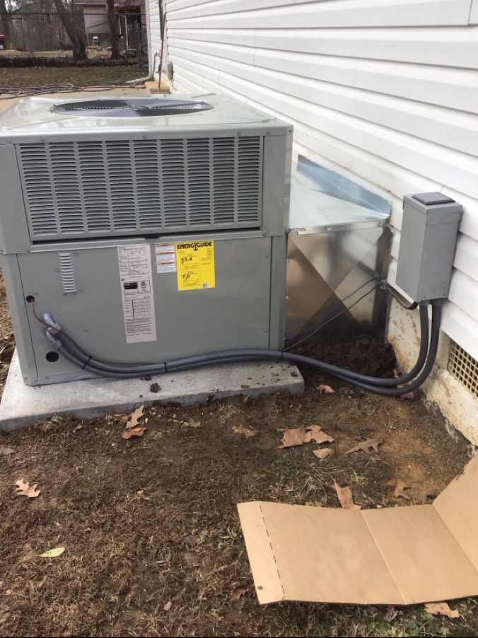 Outdoor HVAC unit beside house siding with conduit box and cardboard on the ground