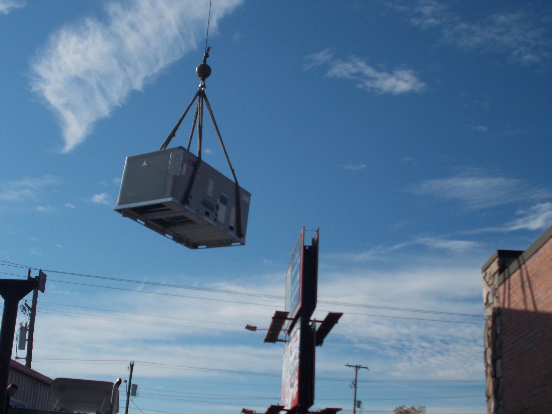 Crane lifting a large gray box-shaped load against a blue sky.