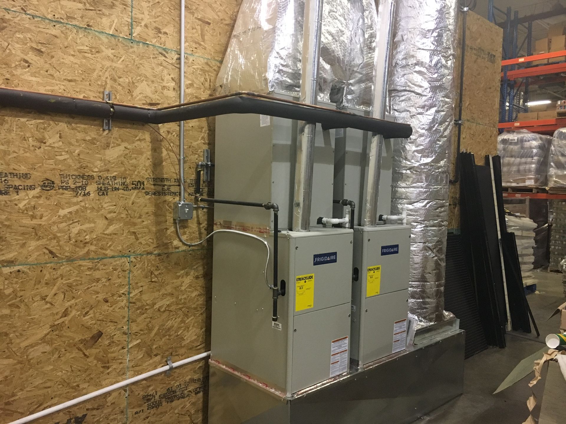 Two gray electrical panels on a wall with black conduits, beside insulated ductwork in an industrial room