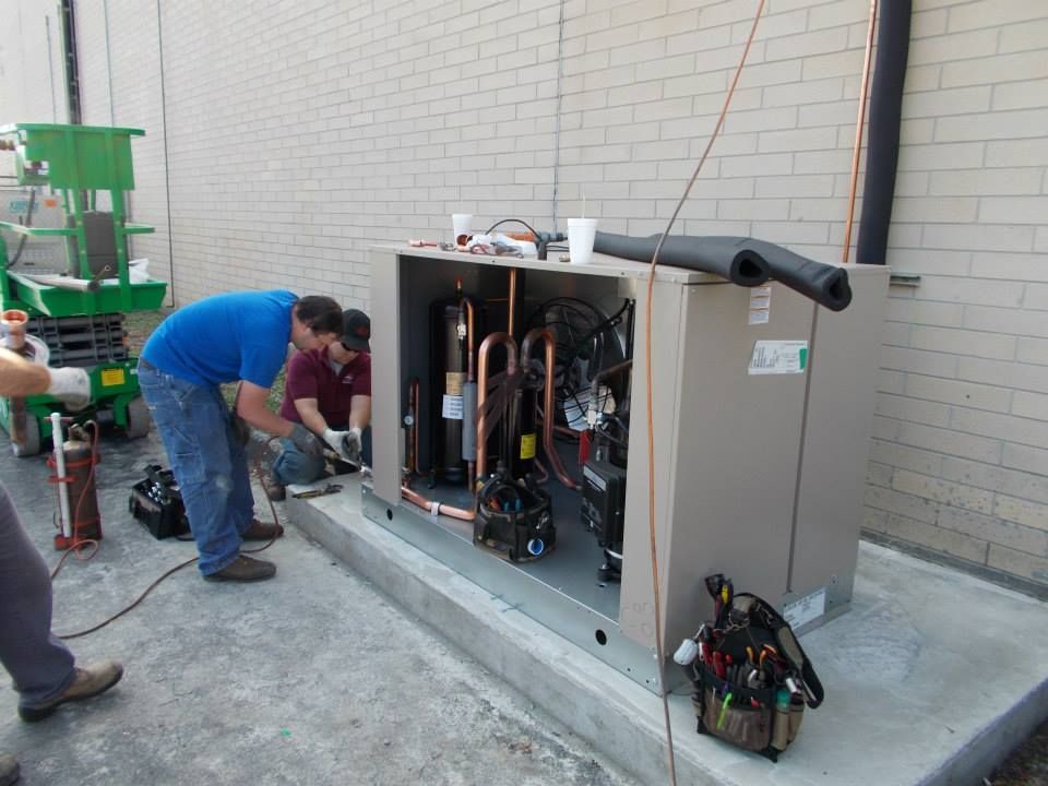 Two men are working on a HVAC machine outside of a building