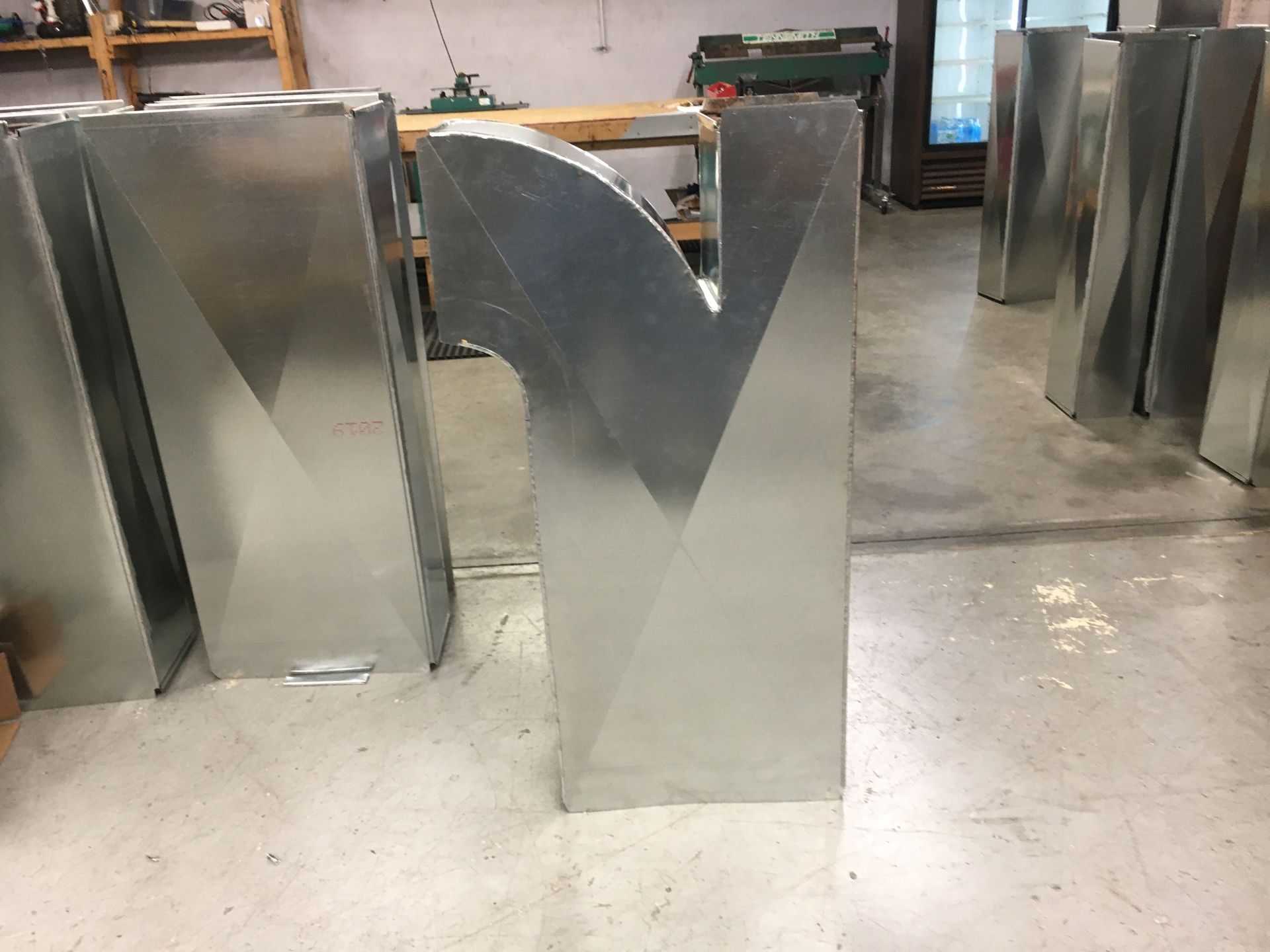 Metal letters in a workshop, including a large shiny V-shaped piece in the center