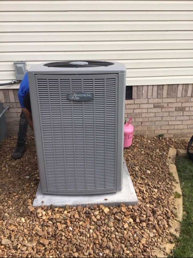 Outdoor HVAC unit on a concrete pad beside a house, with gravel and a worker partly visible behind it.
