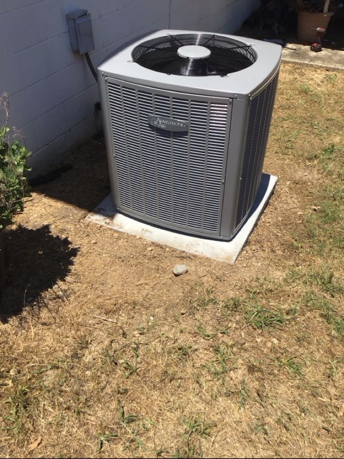 Outdoor air conditioning unit on a concrete pad beside a house, with dry grass around it.