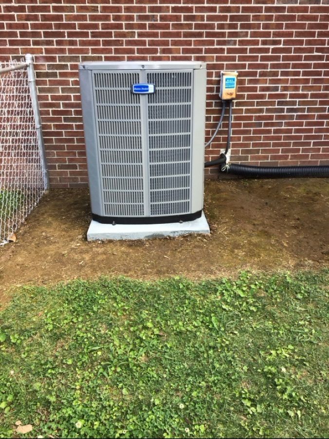 Outdoor air conditioner unit against a brick wall, with an electrical box and hose nearby.