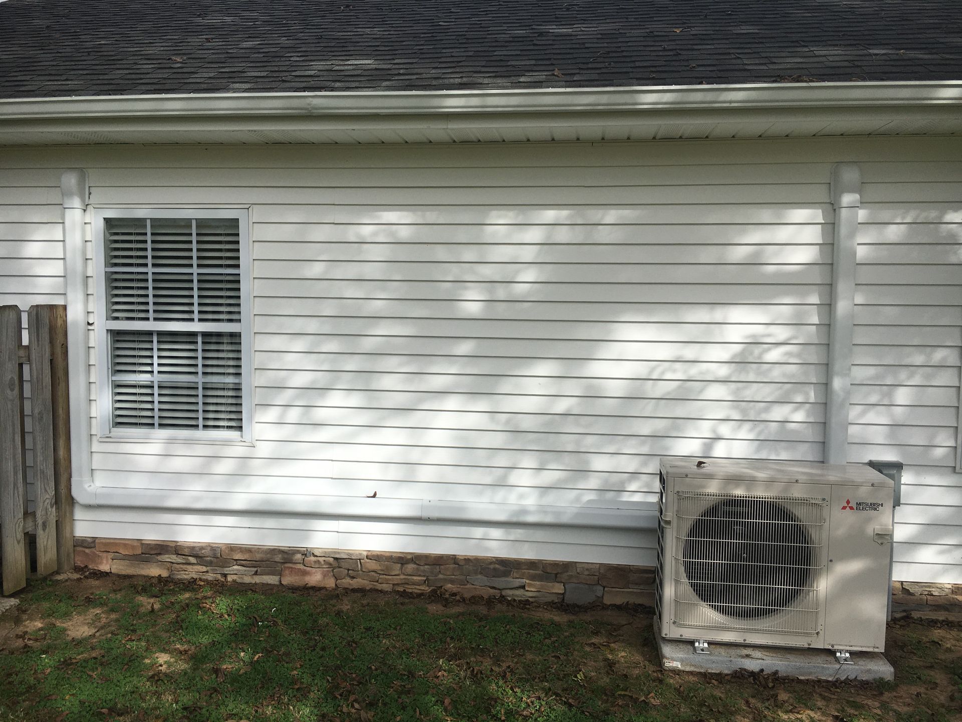 Side of a white house with a window and an outdoor air conditioning unit near the wall.