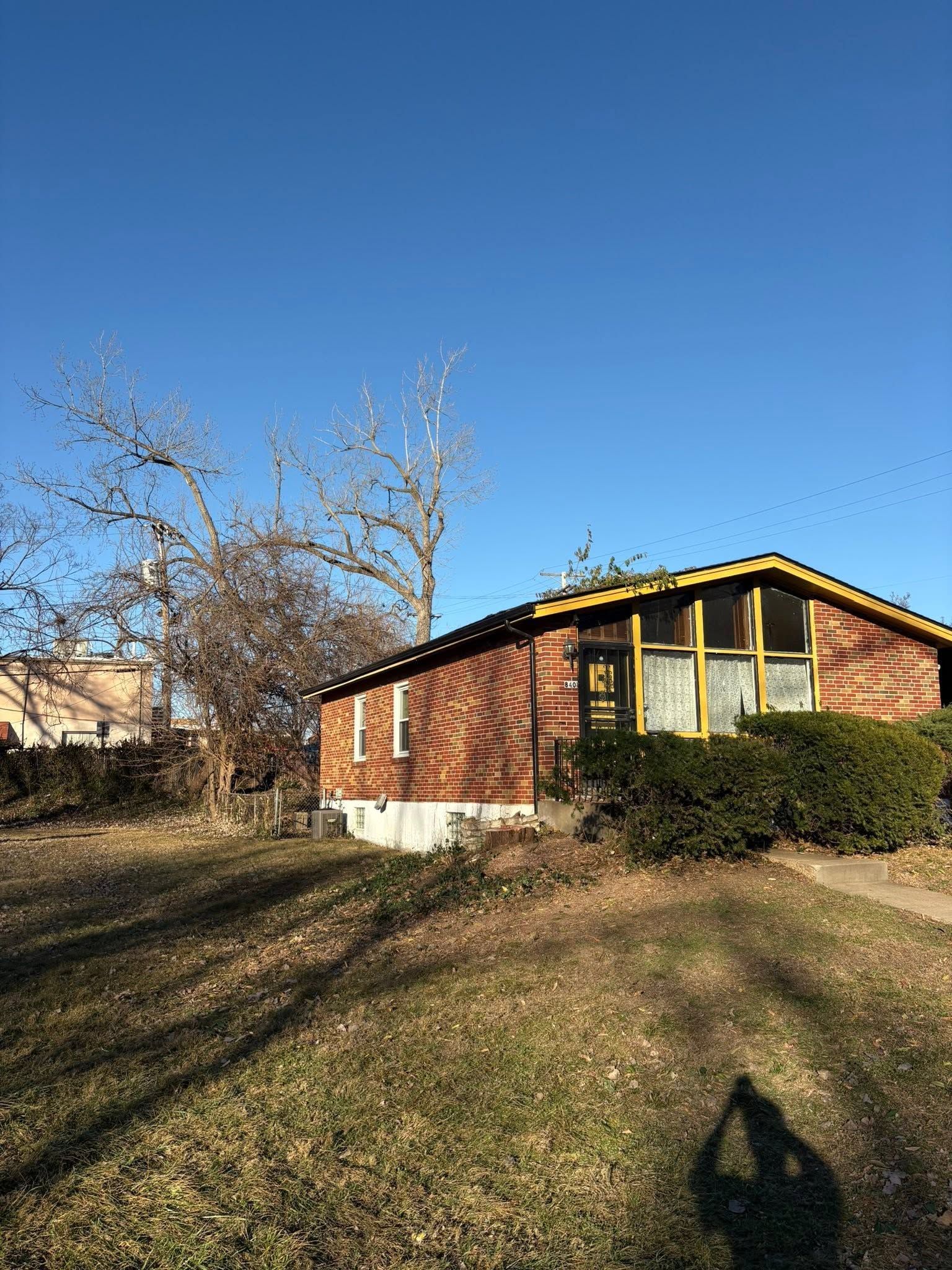 Brick house with yellow trim beside a leafless tree under a clear blue sky