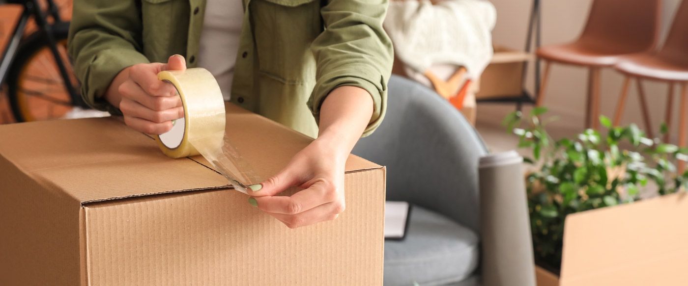 Person sealing a cardboard moving box with packing tape in a living room