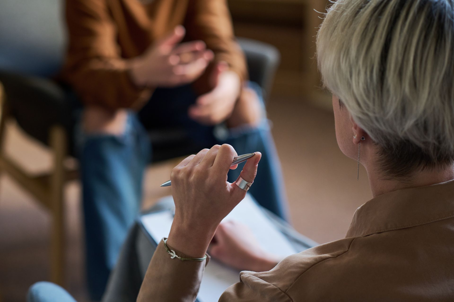 Person sitting with head in hand while another holds out a smartphone, suggesting distress or support