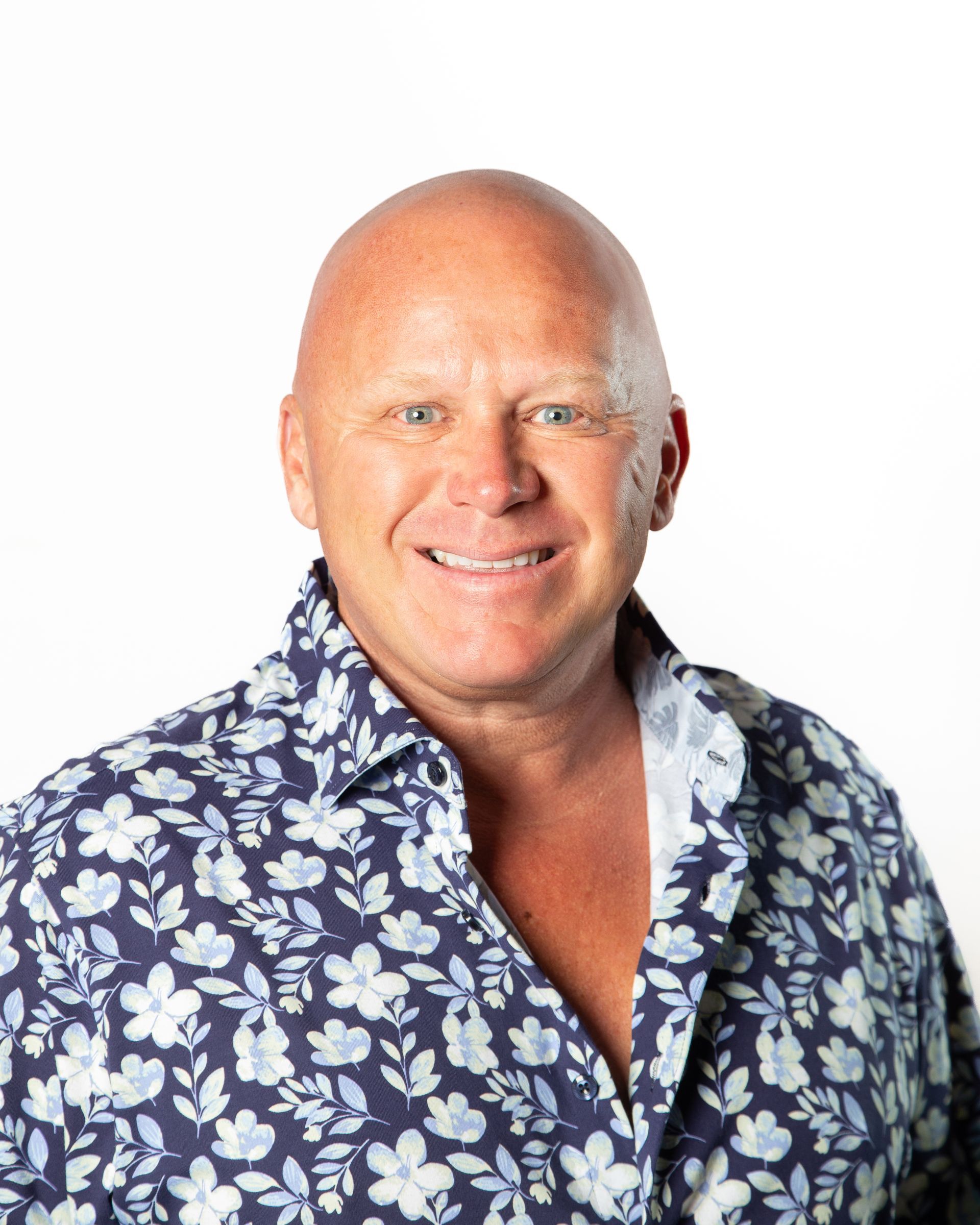 Smiling man in a blue floral shirt against a white background