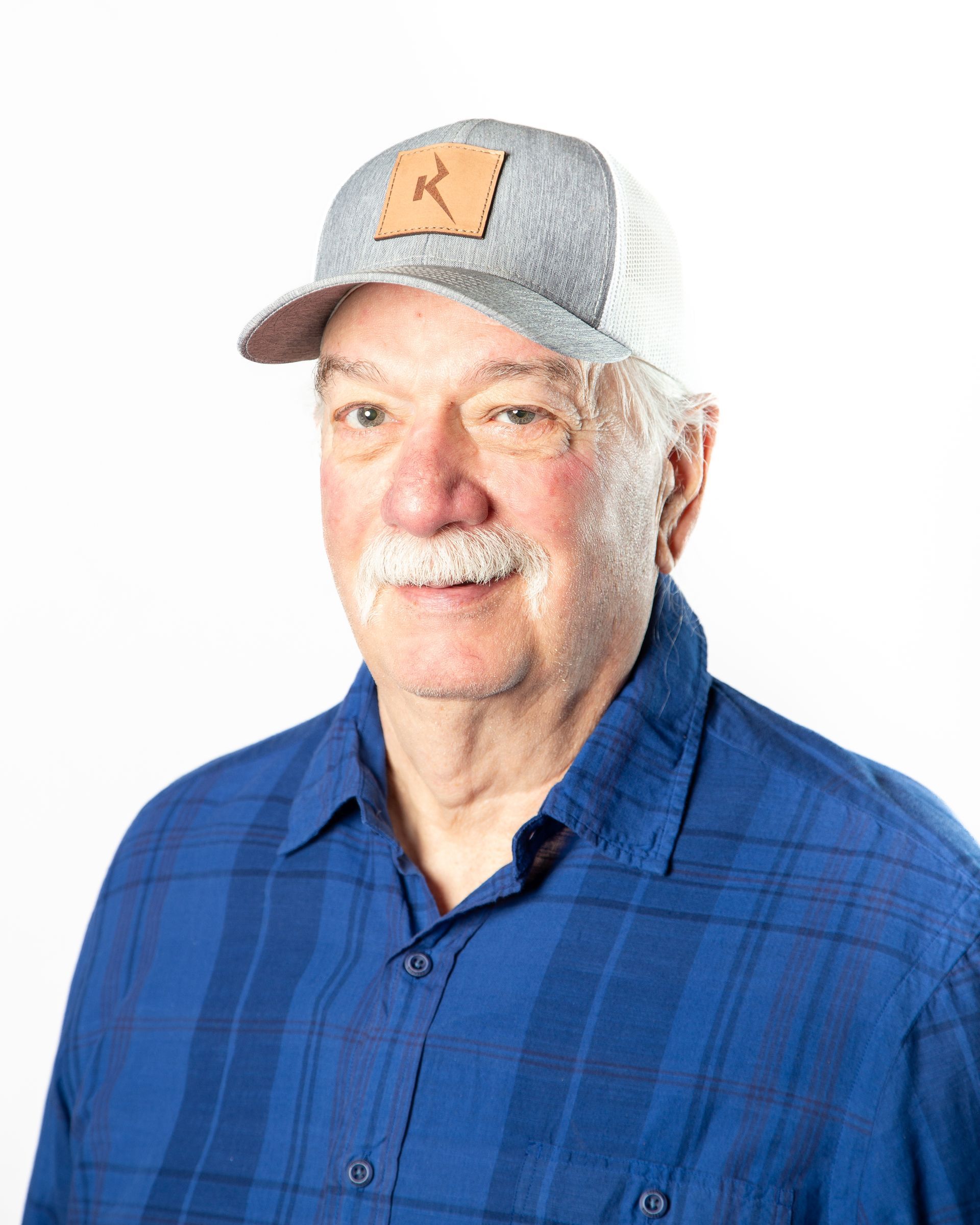 Man in gray cap and blue plaid shirt, smiling against a white background