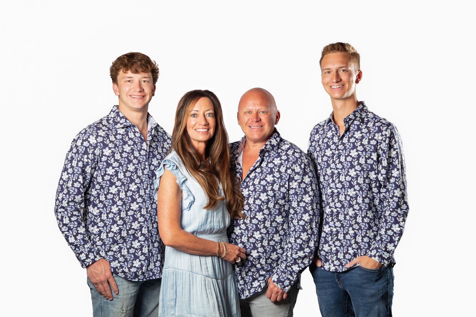 Four people standing together against a white background, wearing matching blue patterned shirts.