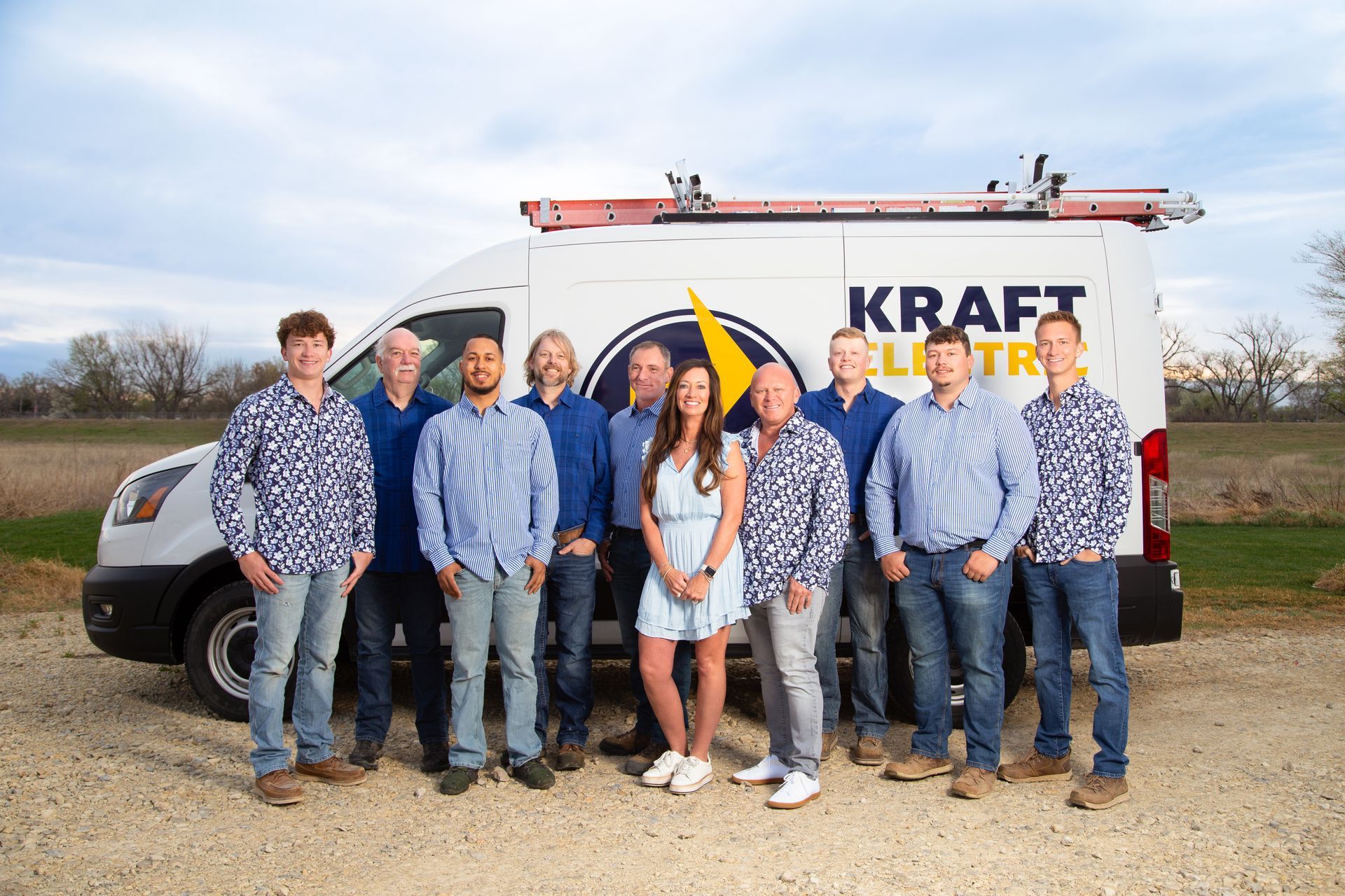Group of nine people standing beside a Kraft-branded van in a gravel lot under a blue cloudy sky