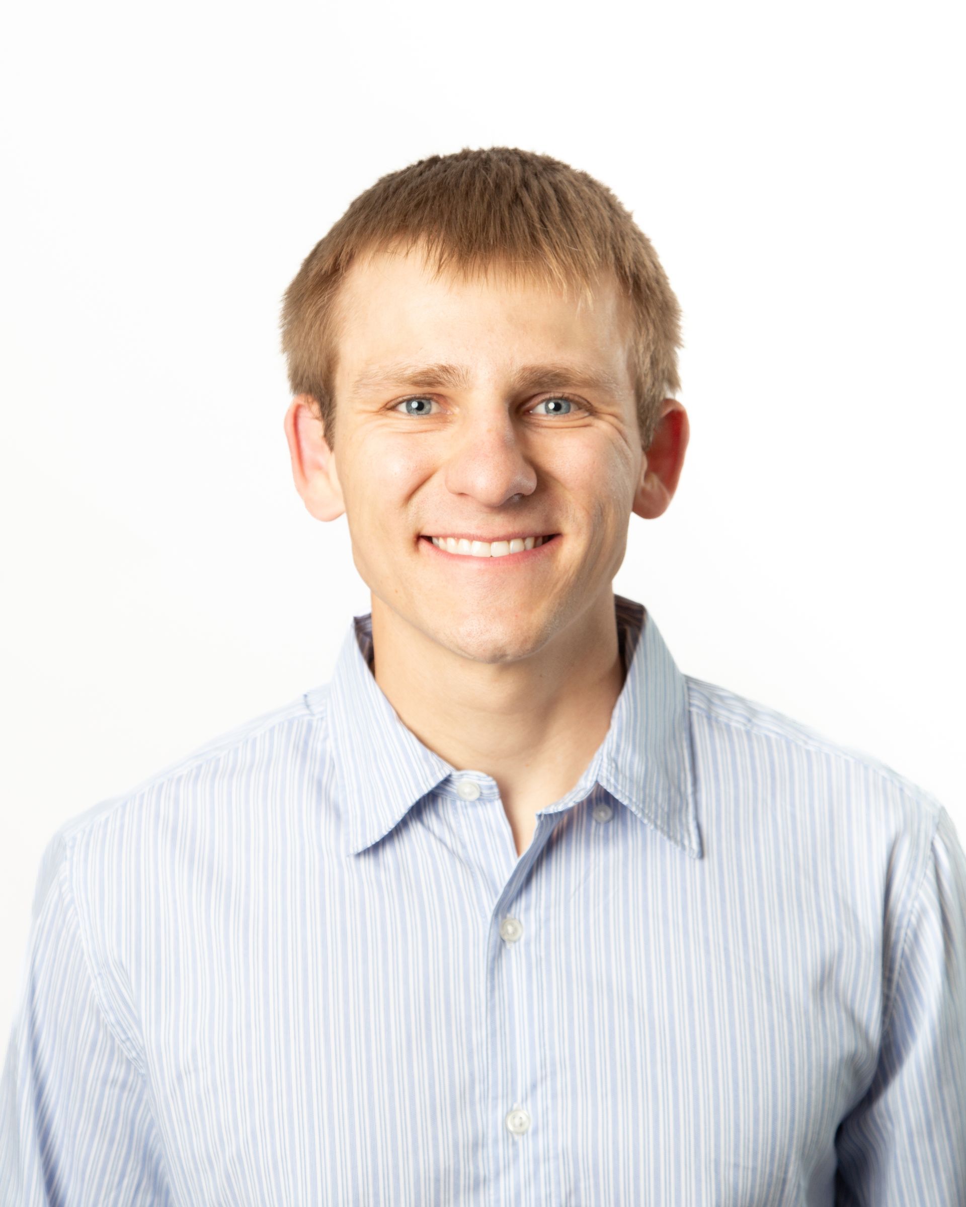 Smiling man in a light blue striped button-up shirt against a white background