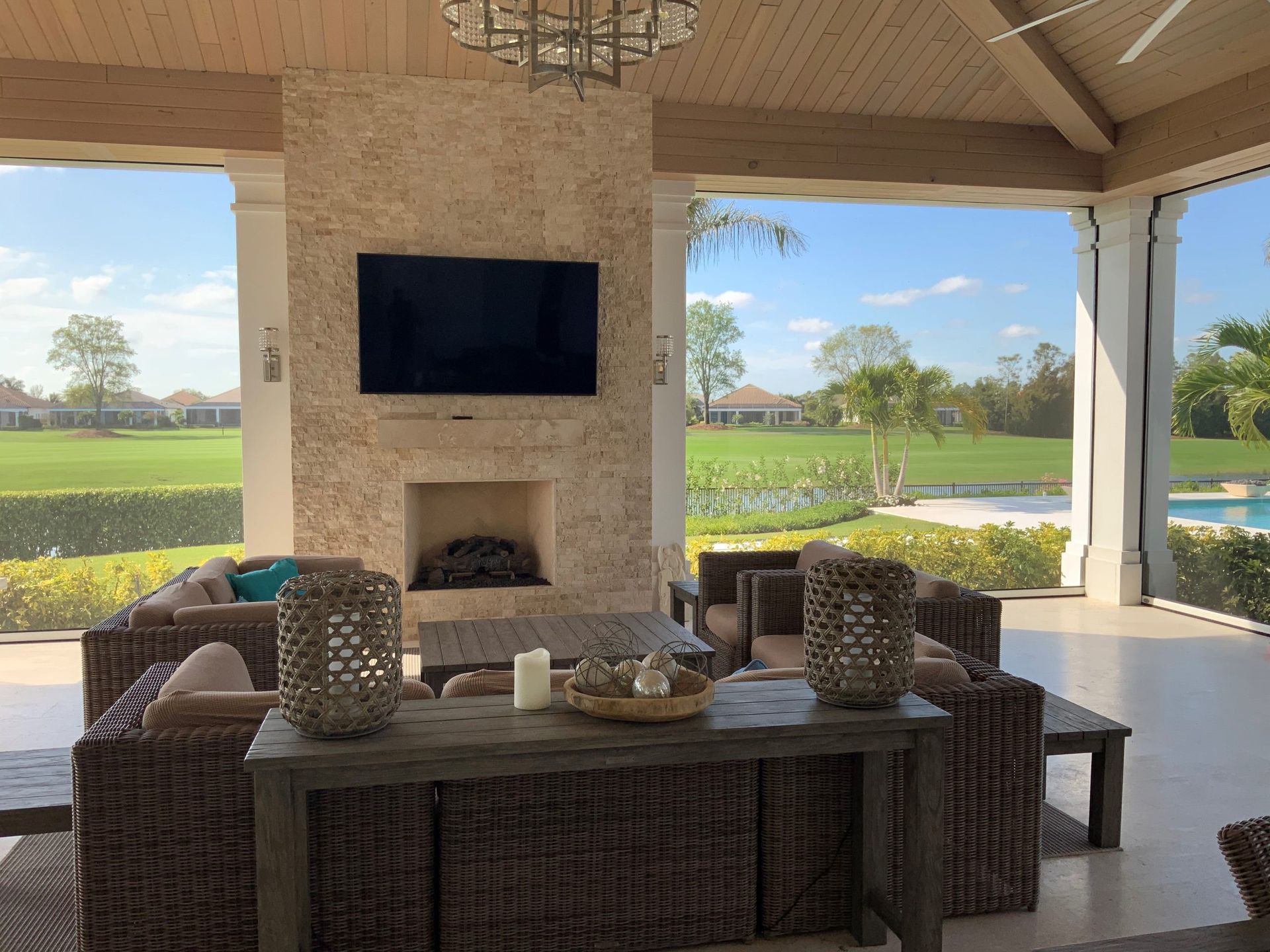 Covered patio with wicker seating, fireplace, and TV overlooking a green golf course