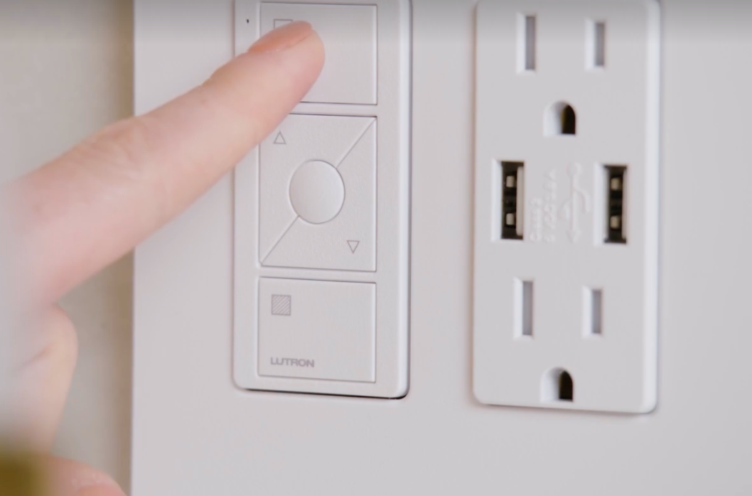 Finger pointing at a wall control next to a white electrical outlet.