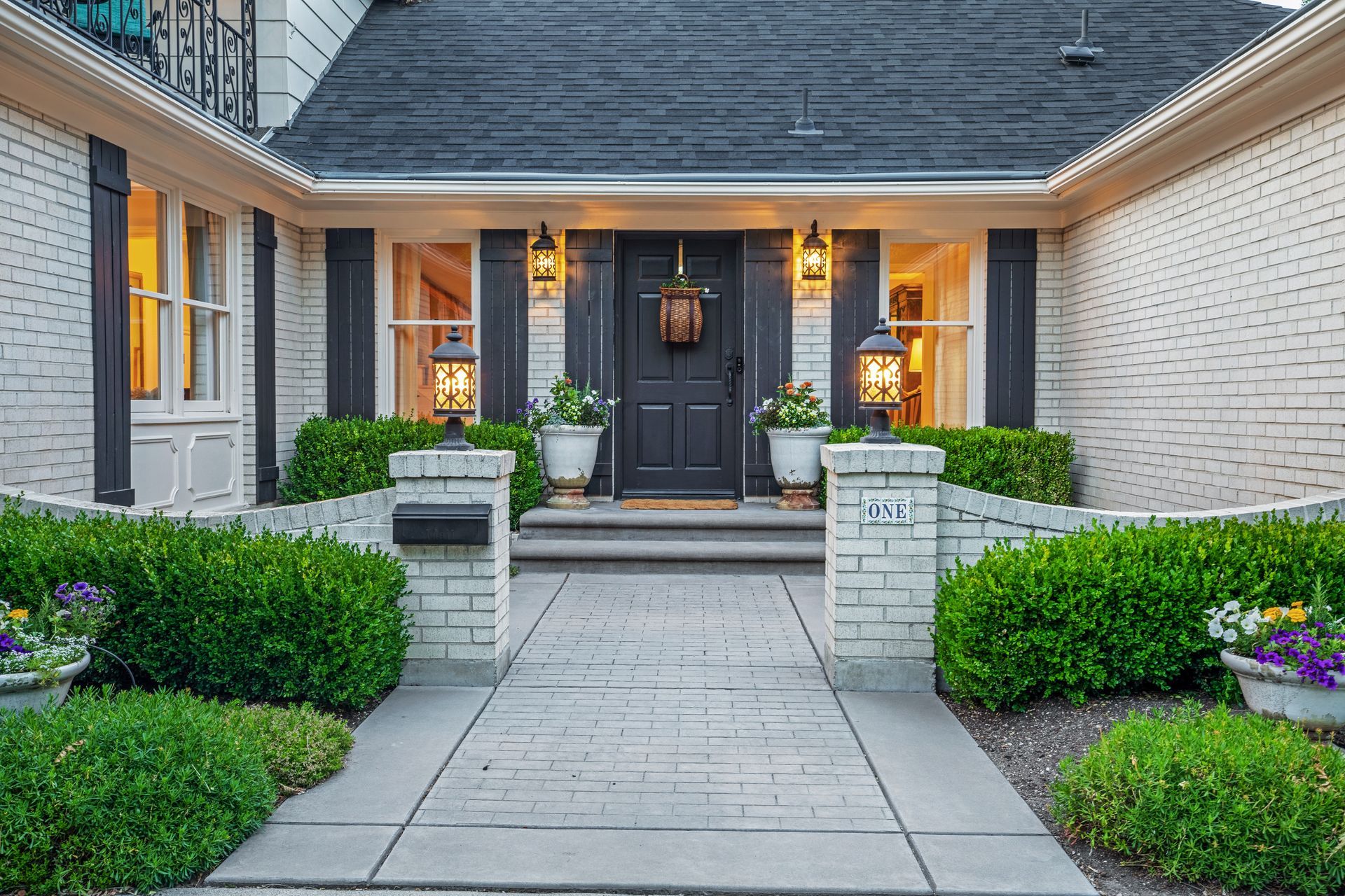 Front entrance of a modern house with a black door, white brick exterior, and landscaped walkway