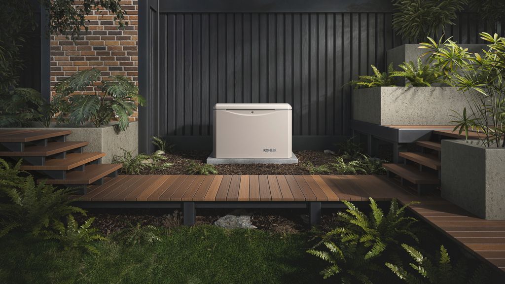 Modern patio with a white outdoor unit centered on a wooden deck, framed by brick, dark siding, and greenery