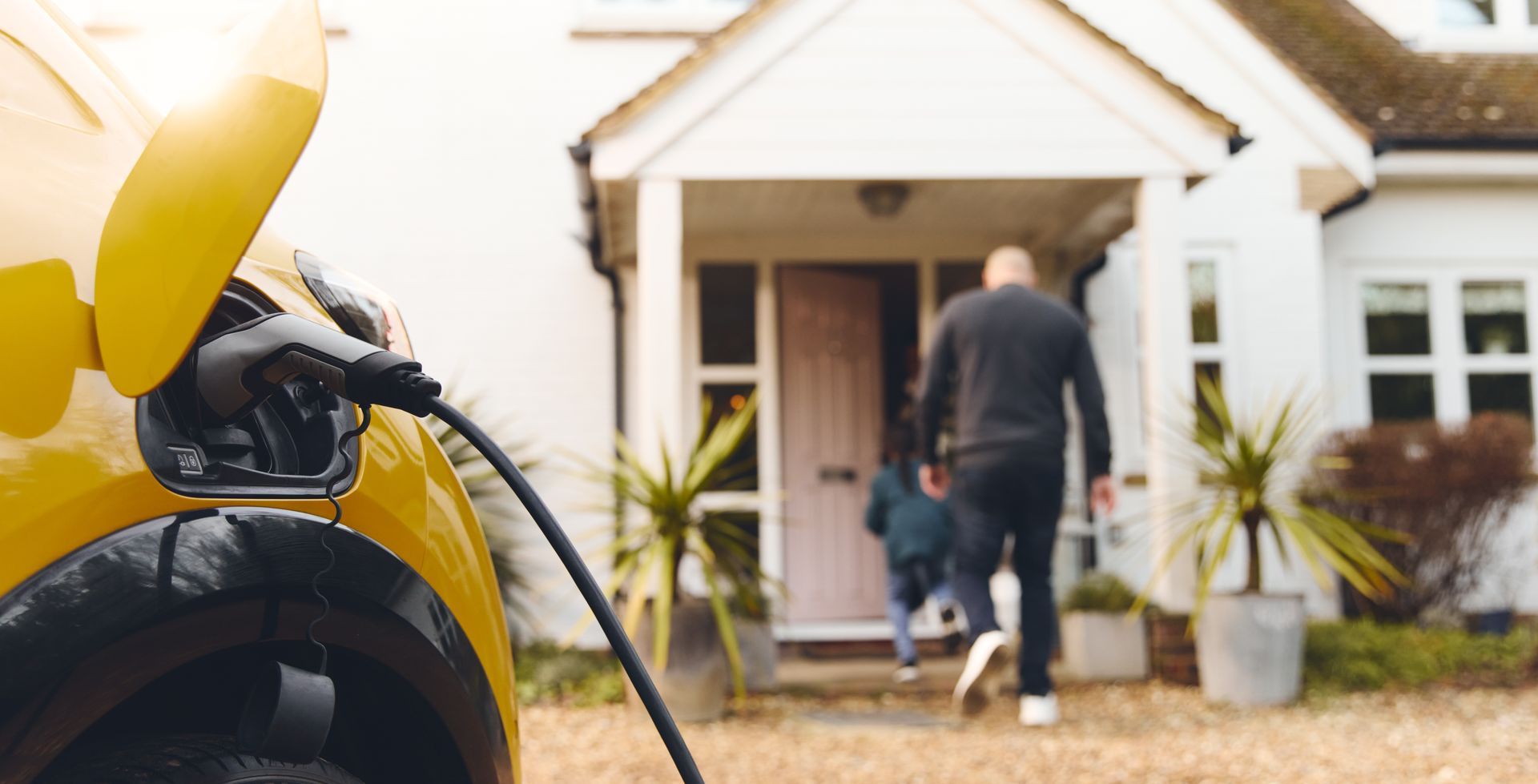 Yellow electric car charging outside a house as two people walk to the front door