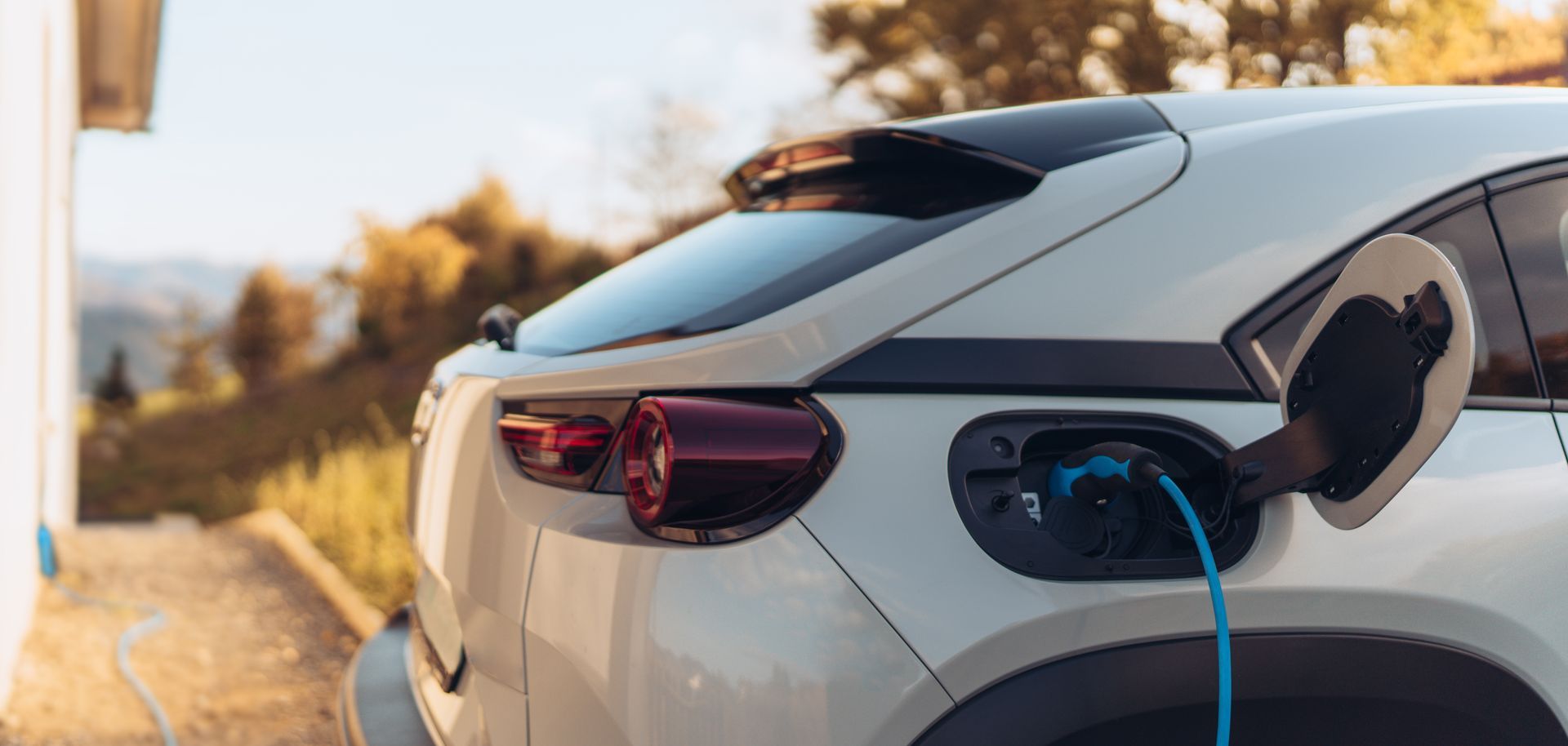 White electric car charging at a roadside station at sunset