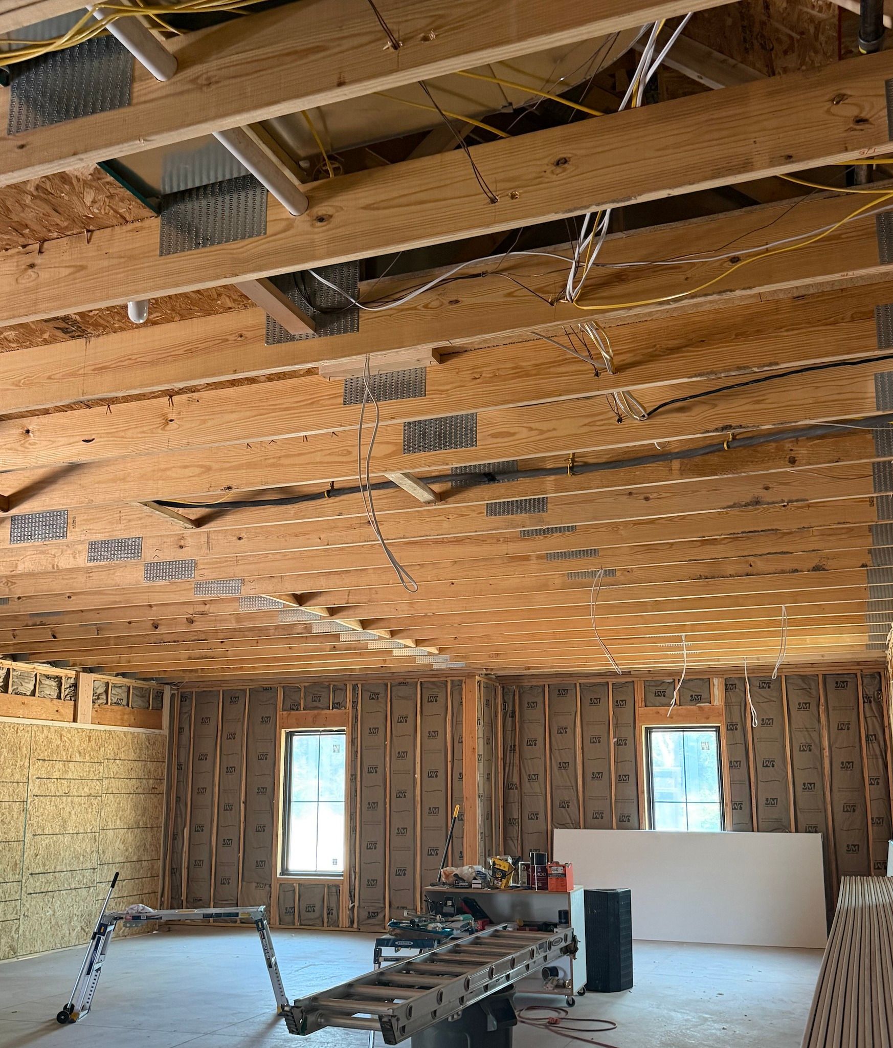 Interior of a house under construction with exposed ceiling beams, insulation, and unfinished walls