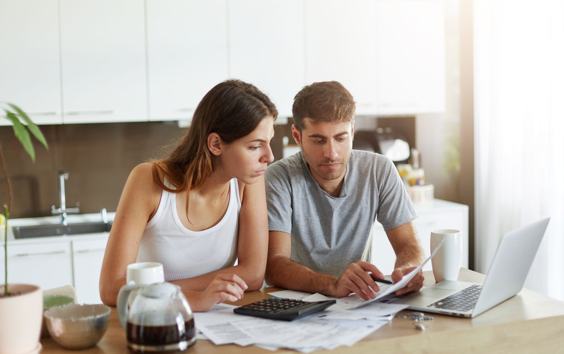 Two people reviewing papers at a kitchen table with a laptop and coffee pot nearby