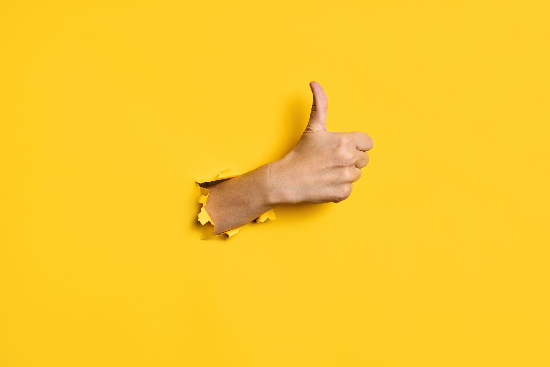 Hand giving a thumbs-up through a torn yellow paper background