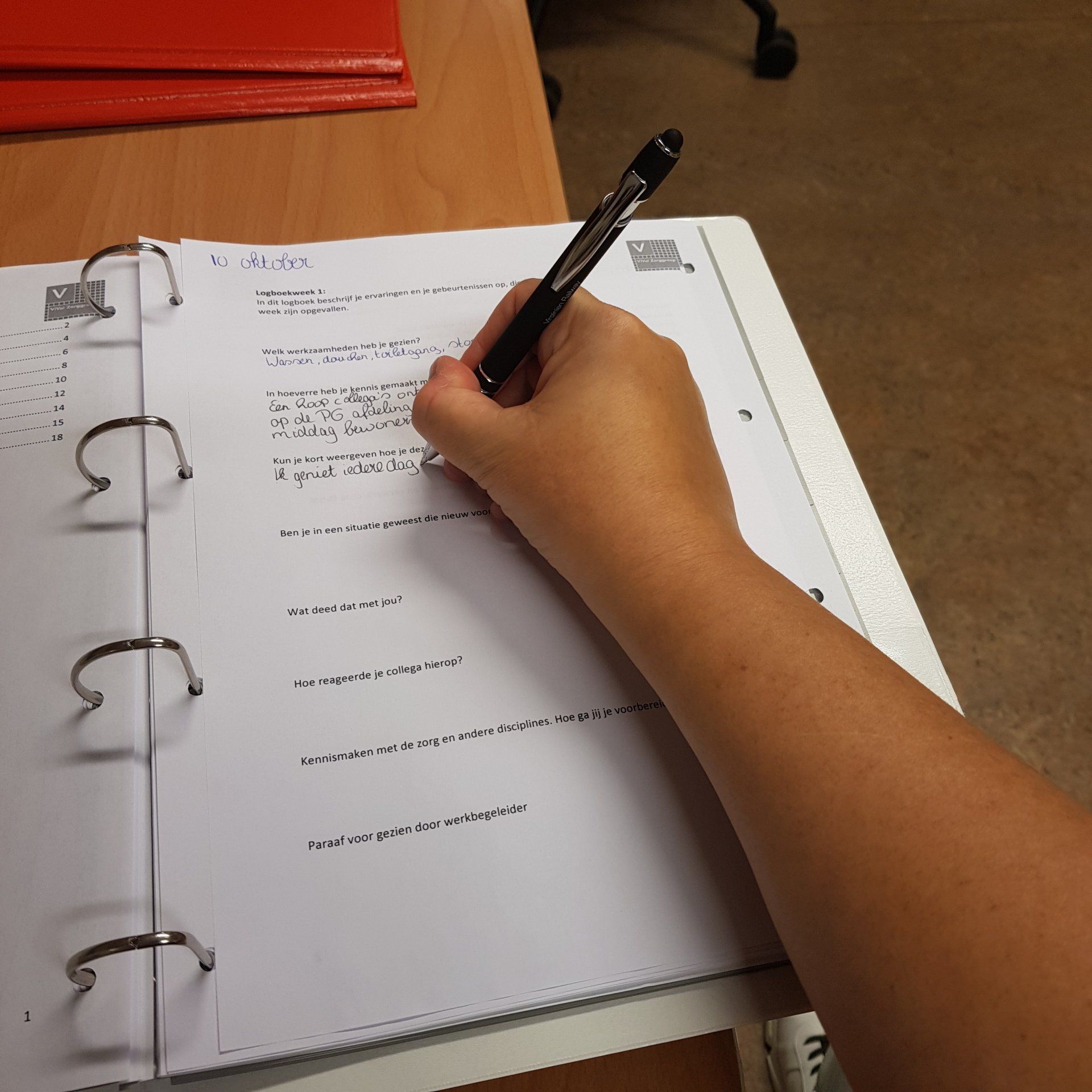 De hand van een persoon die met een pen in een notitieboekje schrijft; studerend in een klaslokaal.