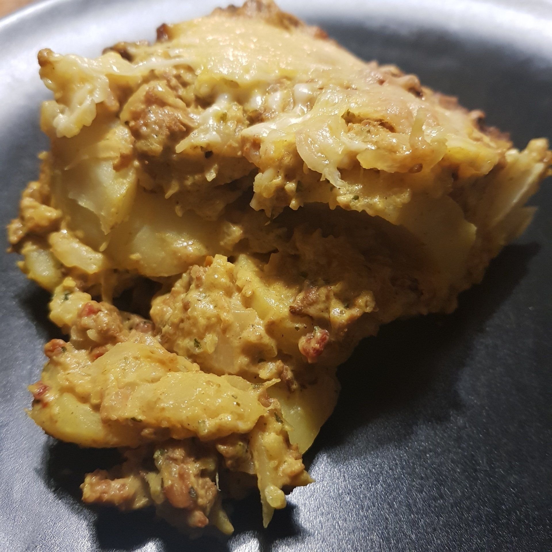 Aardappel- en gehaktschotel op een zwart bord, goudbruin en met een structuur.
