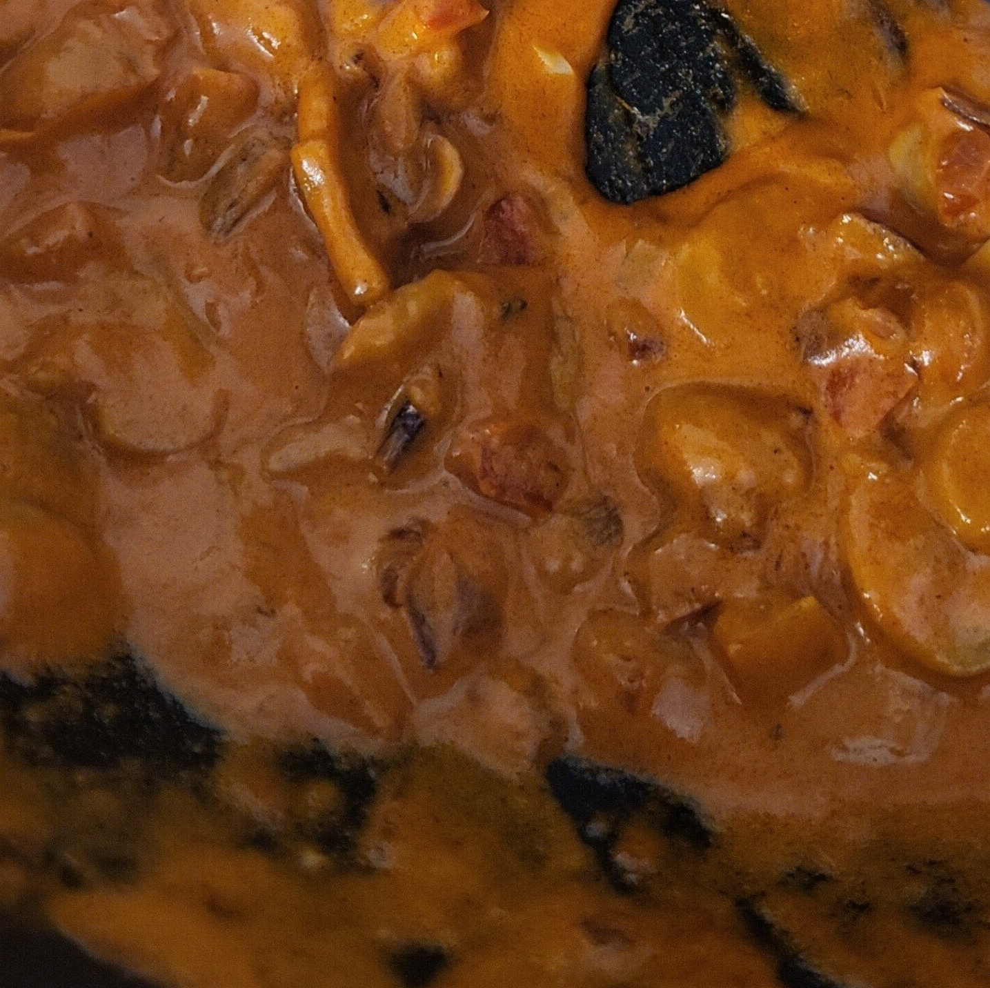 Close-up van romige sinaasappelsaus met verschillende ingrediënten in een donkere pan.