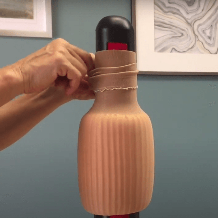 Een persoon wikkelt een bruin, geribbeld voorwerp in een beige stof in een kamer.