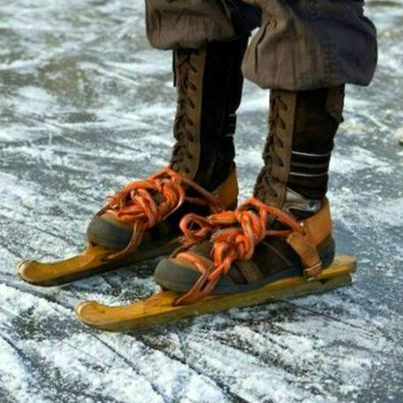 Voeten van een persoon op ouderwetse schaatsen op een besneeuwde, ijzige ondergrond. Oranje veters, bruine laarzen, houten schaatsen.