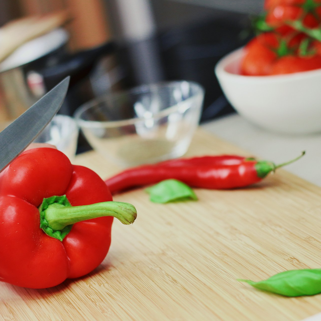 Rode paprika en chilipeper worden op een snijplank bereid met basilicum en een kom tomaten.