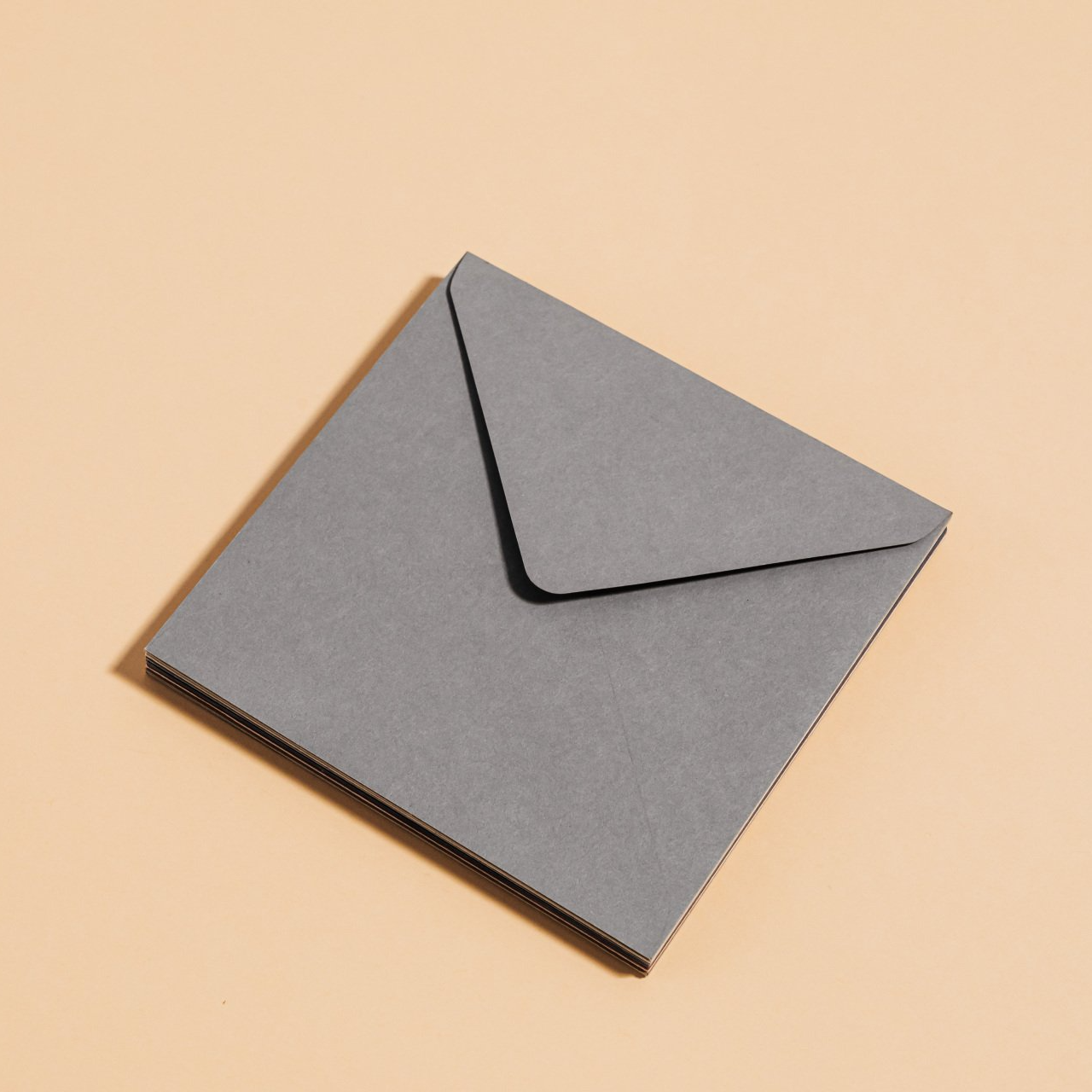 Grijze vierkante envelop, klep gesloten, op een crèmekleurige achtergrond.