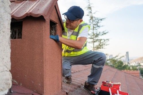 A worker inspecting or repairing a chimney on a rooftop.