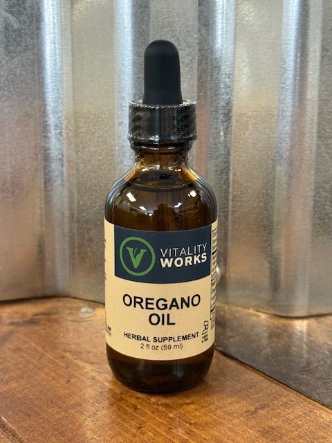 A brown glass bottle of Vitality Works Oregano Oil with a dropper against a corrugated metal backdrop.