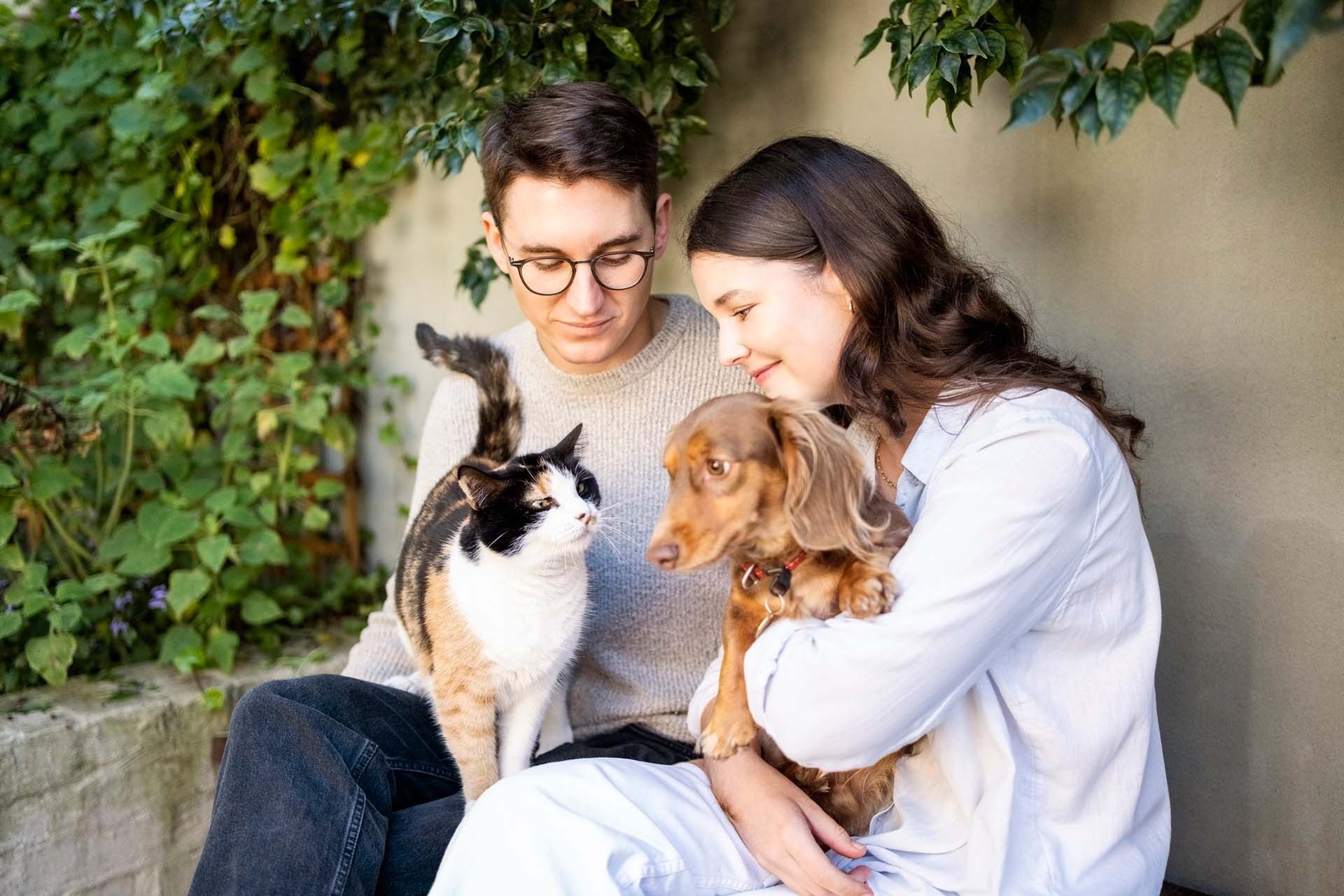 A man and a woman are sitting on a bench with a cat and a dog