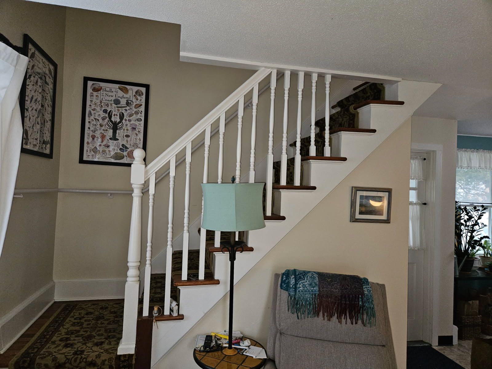 Staircase with white railing. Wall art hangs on the wall. A lamp sits near a chair with a blanket.