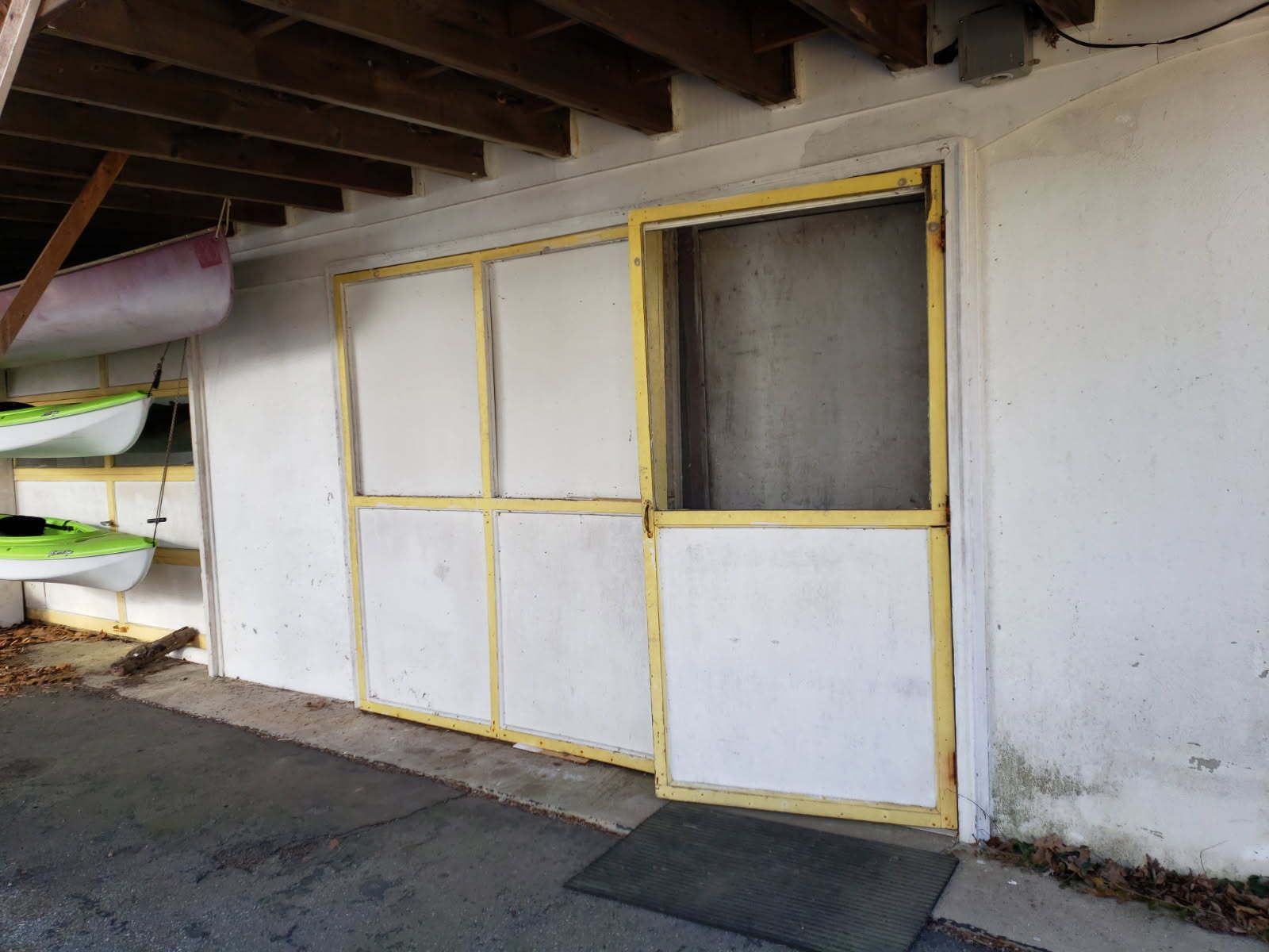 Sliding screen door, off-white with yellow trim, set in a white wall under wooden beams.