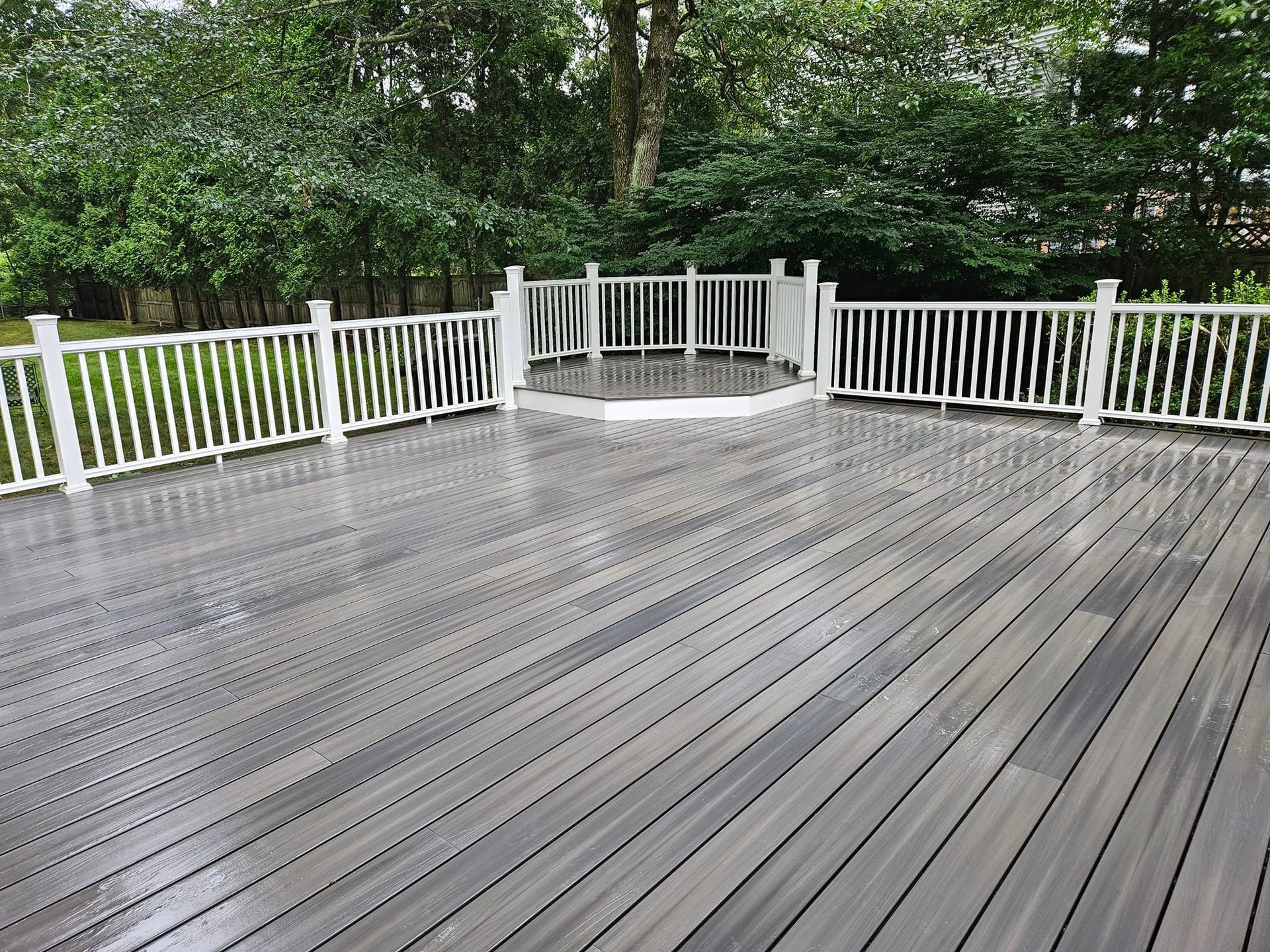 Gray composite deck with white railing, surrounded by green trees.