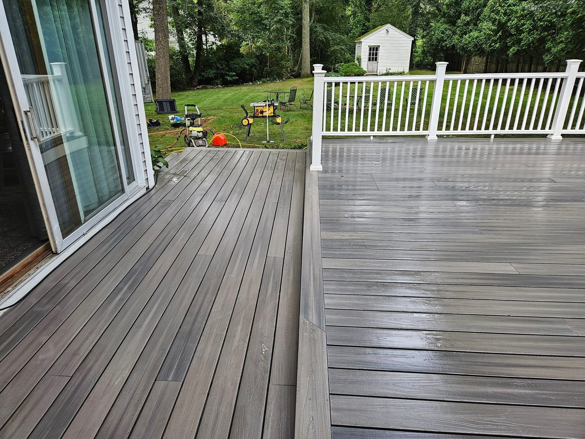 Gray composite deck with a white railing; lawn and small shed in the background.
