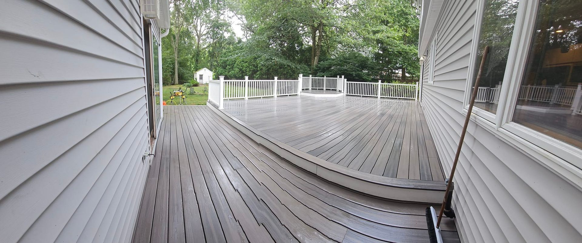 Wooden deck between two buildings with green trees in the background.